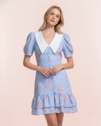 Woman wearing a light blue floral dress with a white collar on a pink background